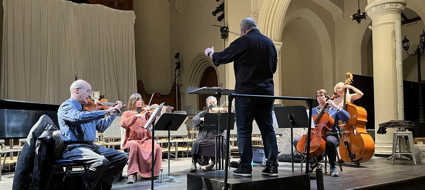 qurtet A conductor leads a string ensemble on stage in a concert hall, with violinists, cellists, and a pianist.