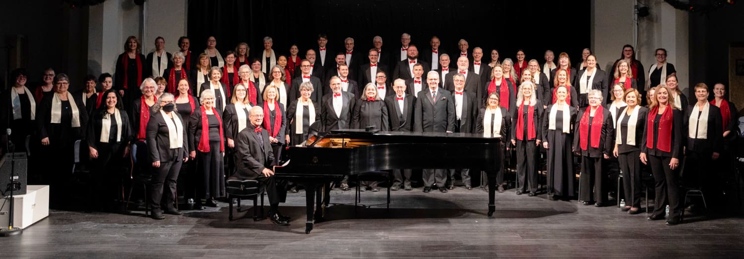 MMSchorale12-2025 A large choir stands on a stage behind a grand piano in the foreground.